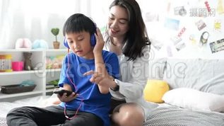 母亲和儿子戴着耳机，用智能手机在家里一起听音乐mov格式视频下载_正版视频编号1430055-摄图网