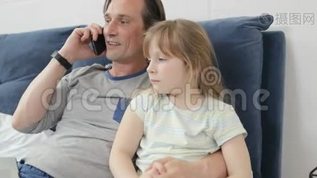 父亲拥抱小女儿，一边打电话，一边快乐地微笑着，一家人坐在床上mov格式视频下载_正版视频编号2493978-摄图网