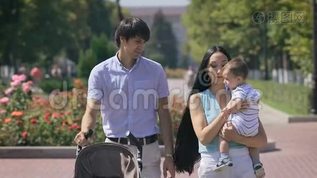 年轻的一家人抱着一个小男孩走在城市公园里。mov格式视频下载_正版视频编号947691-摄图网