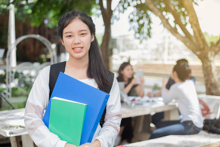 亚洲学生女孩拿着本书在校园