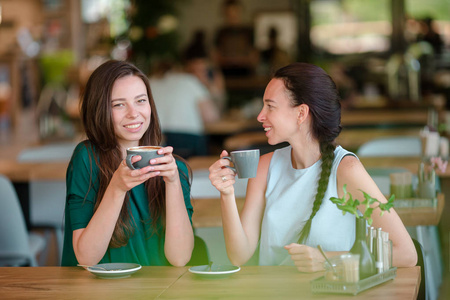 快乐的微笑在咖啡馆的咖啡杯子的年轻妇女。交流和友谊的概念
