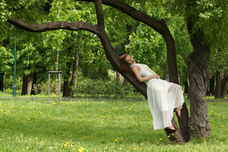 一个漂亮的女孩，在一条长长的白色的裙子靠着一根树枝中夏公园
