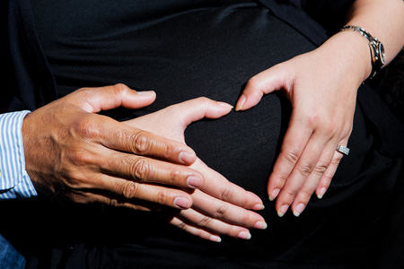 特写怀孕妇人抱着她的手在她隆起的肚子上