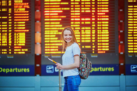 与背包和行李，在国际机场附近飞行信息板进行旅游女孩