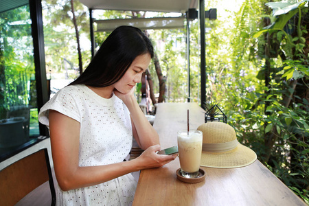 年轻的亚裔女子，坐在咖啡馆里喝咖啡 玩智能手机