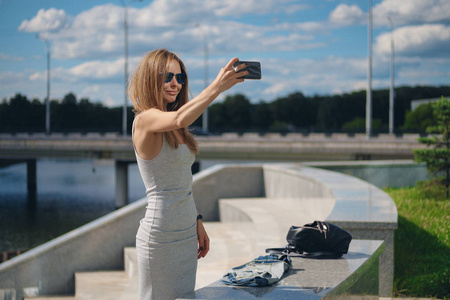 有吸引力的旅游女孩与河岸上背景的自拍照在城市公园