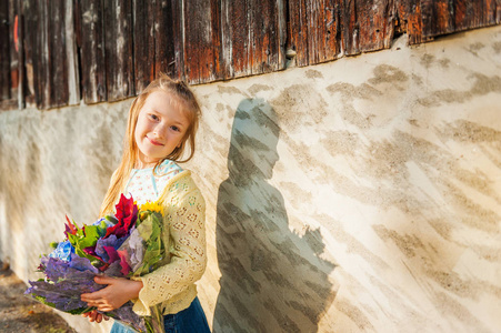 一个可爱的小女孩抱着秋天美丽花束的室外肖像