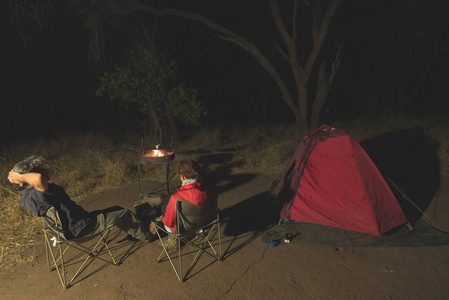 成人的情侣在夜晚的露营地。在南非国家公园探险。在背景中燃烧的篝火和帐篷。色调的图像