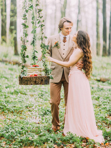 一对新婚夫妇站在挂树桩上的垂直照片, 上面有婚礼上的绿色和白色的蛋糕。幸福刚刚结婚在绿色的春天森林