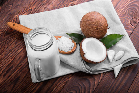 椰子和梅森罐牛奶木背景上一顶视图。含裂纹的椰子和椰片上一袋勺子