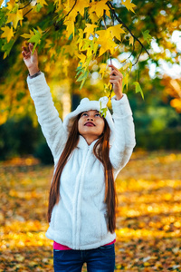 快乐年轻美丽的女人，在晴朗的一天领料秋公园叶子从树上，在白大衣在日落公园里的年轻女子