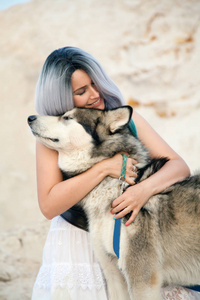 美丽的年轻女老板和她可爱的快乐小狗阿拉斯加雪橇犬在沙漠中猎物的白色沙滩