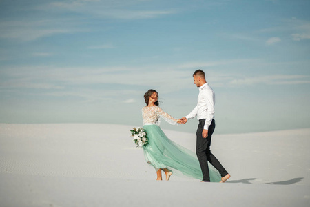 新娘和新郎握着的手，微笑着赤脚行走在沙漠