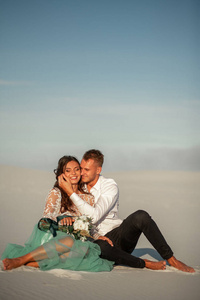 新娘和新郎赤脚坐在白色的沙滩，在沙漠 拥抱和 