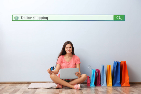 网上购物的概念。带信用卡和笔记本电脑的年轻妇女在家中坐在地板上