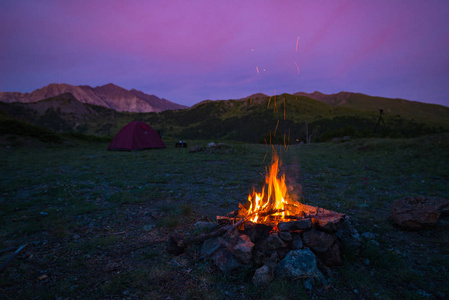 帐篷和燃烧的篝火黄昏在山上。夏天的冒险与探索在阿尔卑斯山。选择性专注于火，色彩斑斓的天空