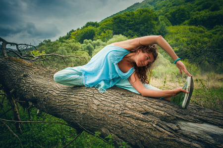 年轻女子练习瑜伽户外在山上的巨大落树上