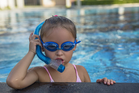 一个快乐的年轻女孩，在戴着护目镜和浮潜的游泳池边放松