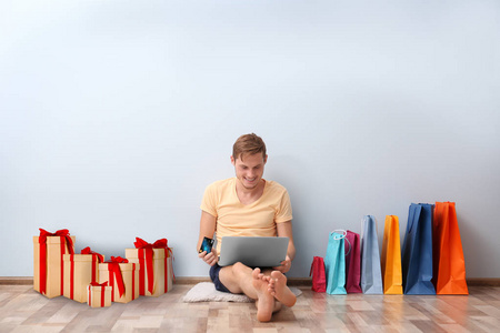 网上购物的概念。男子坐在笔记本电脑和购买附近的墙壁在家