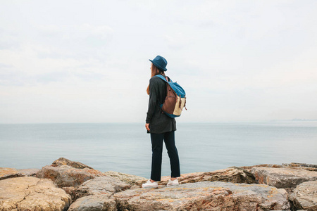 旅行者的女孩与一个背包在海边戴着帽子。旅游，休闲，徒步旅行