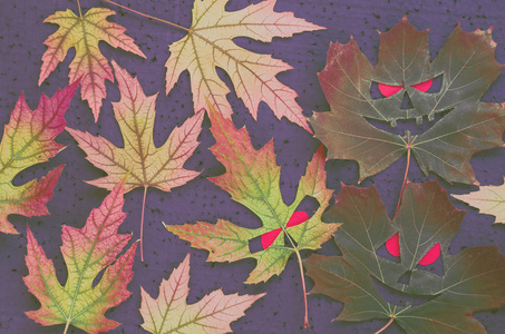 在万圣节风格枫暗秋季模式叶形式的的脸上红红的眼睛在黑色背景上。色调的图像