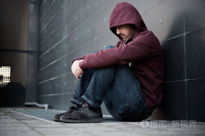 绝望孤独的人坐在墙上在城市的街道