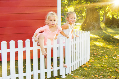 两个小女孩在白色的栅栏，在操场上对阵公园或绿色的森林