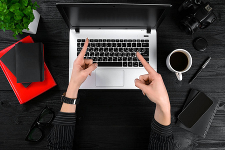 业务和技术主题 显示对背景笔记本电脑的姿态在桌子上的一件黑色衬衫的女人的手