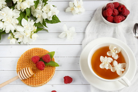 茉莉花与薄华夫饼配蜂蜜和树莓光木背景上的杯茶