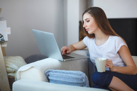 年轻的女人坐在她家沙发上的笔记本电脑