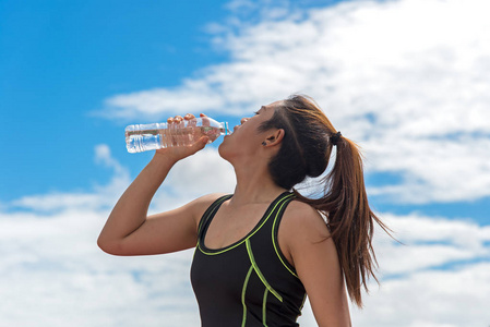 运动运动后，回到地面蓝色天空手持一瓶水的女人。健康概念