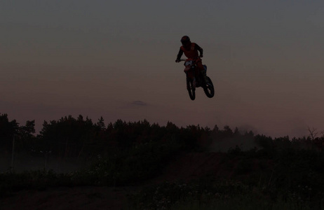 摩托车越野赛车手跳上这座山在夕阳的模糊的轮廓