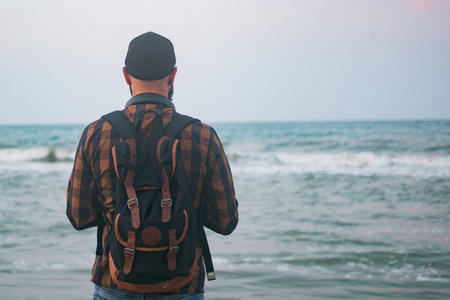 一个年轻的白人游客男子站海洋背景黎明时分。旅游和生活方式的概念