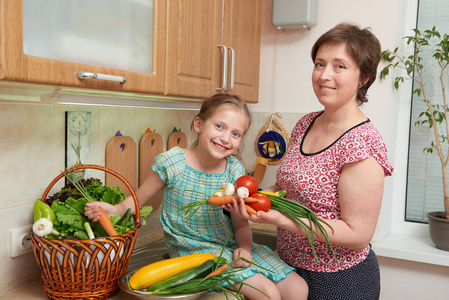 母亲和女儿提着篮子的蔬菜和新鲜水果在厨房内饰。父级和子级。健康食品的概念