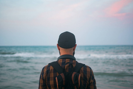 一个年轻的白人游客男子站海洋背景黎明时分。旅游和生活方式的概念