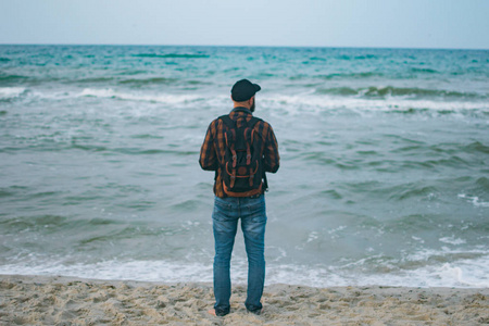 一个年轻的白人游客男子站海洋背景黎明时分。旅游和生活方式的概念