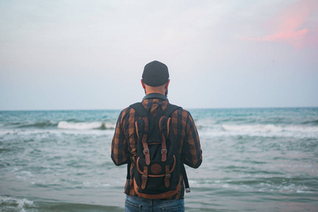 一个年轻的白人游客男子站海洋背景黎明时分。旅游和生活方式的概念