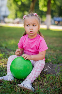可爱的孩子小女孩坐在公园的草地上，玩绿色球和微笑