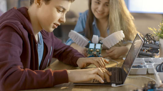 女孩和男孩程序功能齐全机器人与笔记本电脑为他们