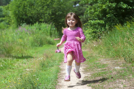 可爱的小女孩，在粉红色的连衣裙在森林里跑。阳光灿烂的日子