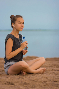 在沙滩上，选择性焦点体育女孩在锻炼期间喝水。那个女孩在健身户外活动期间喝水