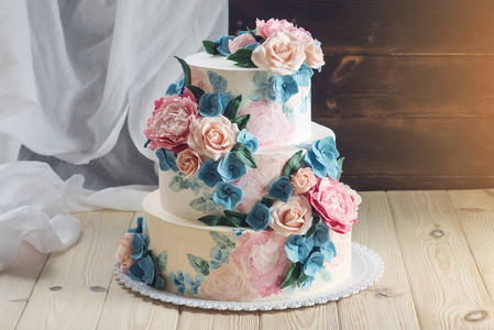 一个美丽的家庭婚礼三层蛋糕装饰着粉红玫瑰和蓝色的花朵，在一个乡村风格木制的桌子上