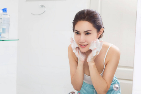 女人很高兴洁净皮肤与泡沫在浴室