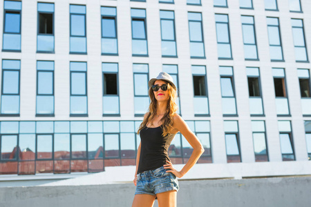 阳光灿烂的生活方式时尚的年轻时尚时髦的女人走在街上，穿着新潮的衣服和帽子的肖像