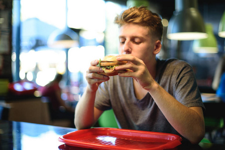 在手中的一个少年人坐在一家快餐店美味，高大的汉堡
