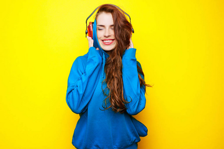 年轻漂亮的女孩 Dj 在蓝色夹克在黄色的背景和有乐趣的红色耳机听音乐