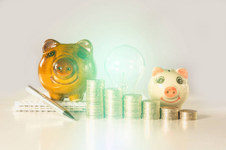 节能灯泡与储钱罐和成堆的硬币在桌上。金融和储蓄的概念