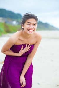 快乐 爱笑的年轻女孩，在紫色的裙子，在海滩上笑