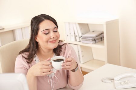 年轻的商务女性在现代办公室享受咖啡