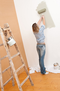 家里的改进 开朗女人带漆滚子和梯子